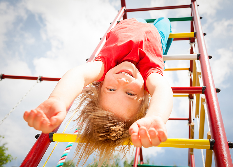 Happy girl hanging from a jungle gym in a summer garden